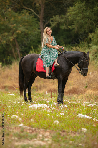 Woman in a dress rides an amazon on a black horse