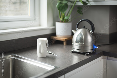 Quadro su tela A boiling kettle next to a white cup with a tea bag on it and a spoon on a kitch