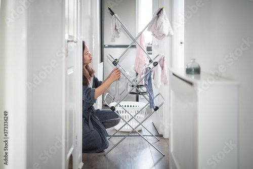 Canvas-taulu An Asian woman wearing a bathrobe hangs clothes on a drying rack on a corridor n
