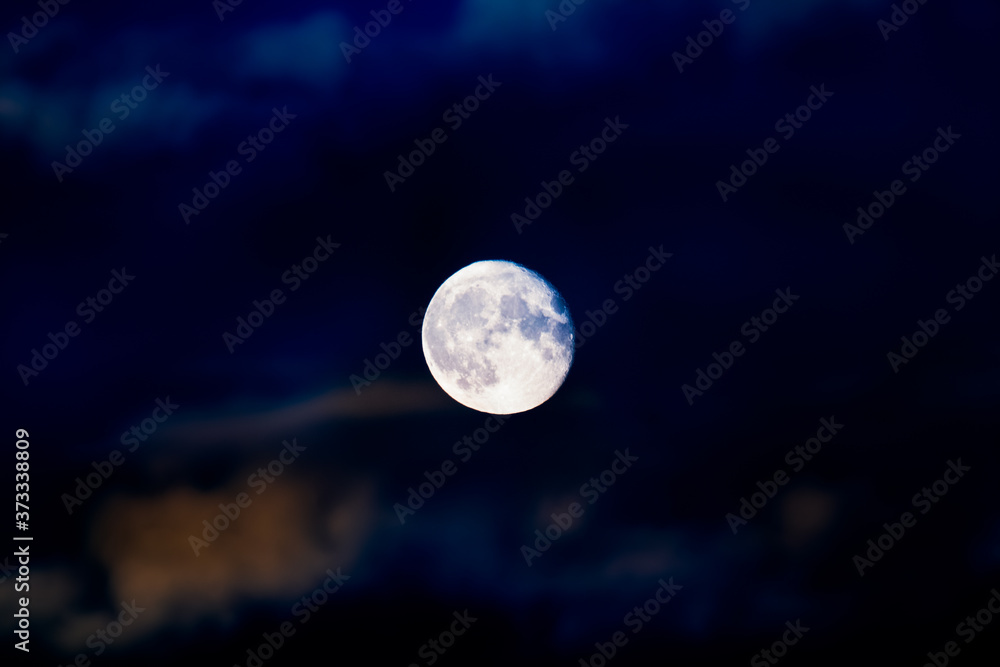 Bright colorful full moon close-up on cloudy vibrant blue lights night sky with colorful clouds. Mystic nighttime northern lights sky with large moon