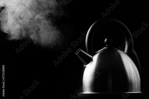 Hot modern kettle boiling on black background with steam rising to the light