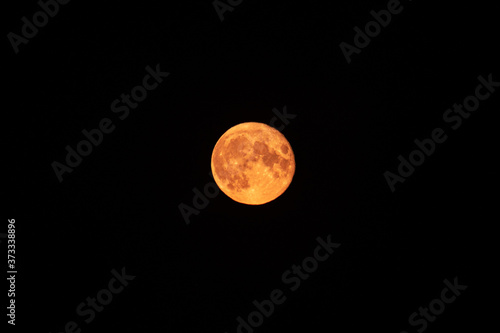 Bright red orange full moon rising up on dark night sky. Mystic nighttime black sky with large moon, dark tranquility