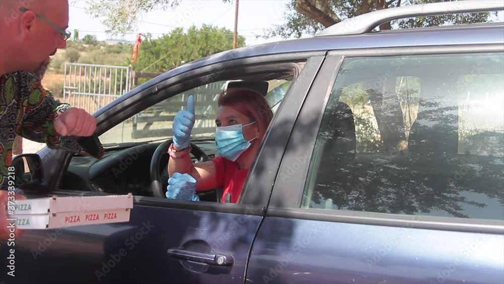 female pizza delivery boy delivering two cartons of Italian pizza directly from the car window with a health mask over his mouth to prevent the covid19 virus female pizza delivery boy delivering two cartons of Italian pizza directly from the car window with a health mask over his mouth to prevent the covid19 virus