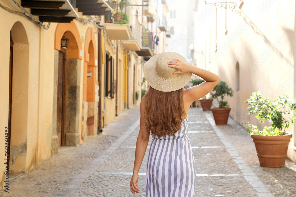 Rear view of tourist woman walking in the old town of Cefalu in Sicily, Italy