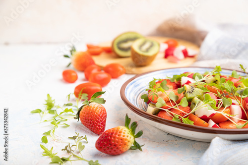 Vegetarian fruits and vegetables salad of strawberry, kiwi, tomatoes, microgreen sprouts on white concrete background. Side view, selective focus.