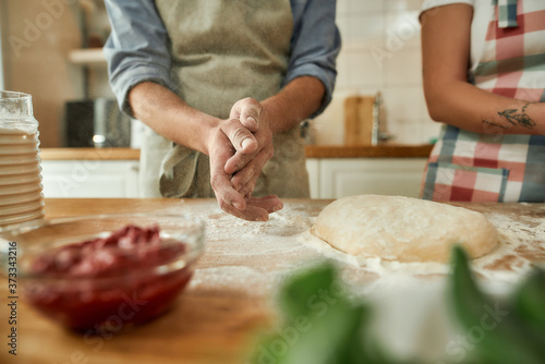 Cropped shot of couple making pizza together. Young man in apron preparing the dough using flour while woman helping him. Hobby, lifestyle