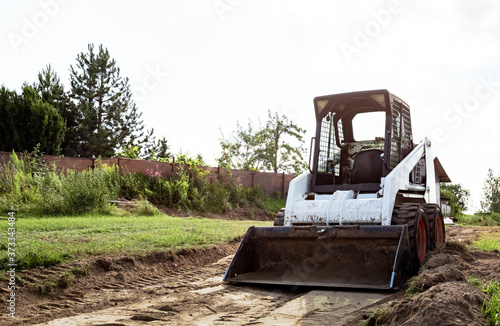 A skid steer loader clears the site for construction. Land work by the territory improvement. Machine for work in confined areas. Small tractor with a bucket for moving soil and bulk materials. © Hanna