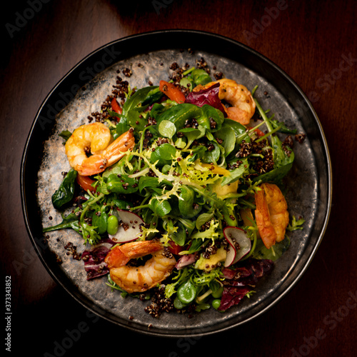 Shrimps salad with cherry tomatoes, cucumeber, avocado, lettuce and pomegranate on dish. Healthy seafood concept. Tasty grilled prawn shrimp and mix vegetable salad on black wood