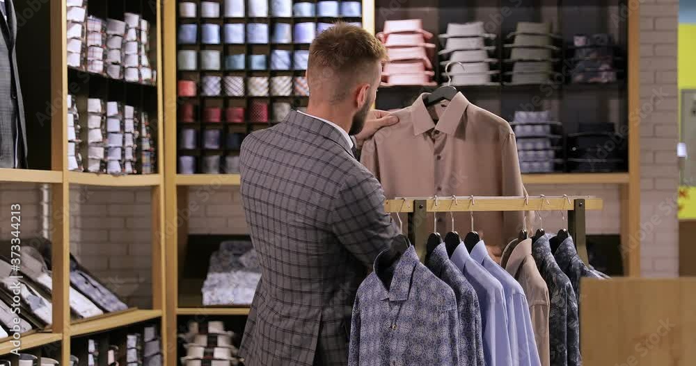 A business man in a store selects a men's shirt and takes it off the hanger. A business man in a store selects a men's shirt and takes it off the hanger.