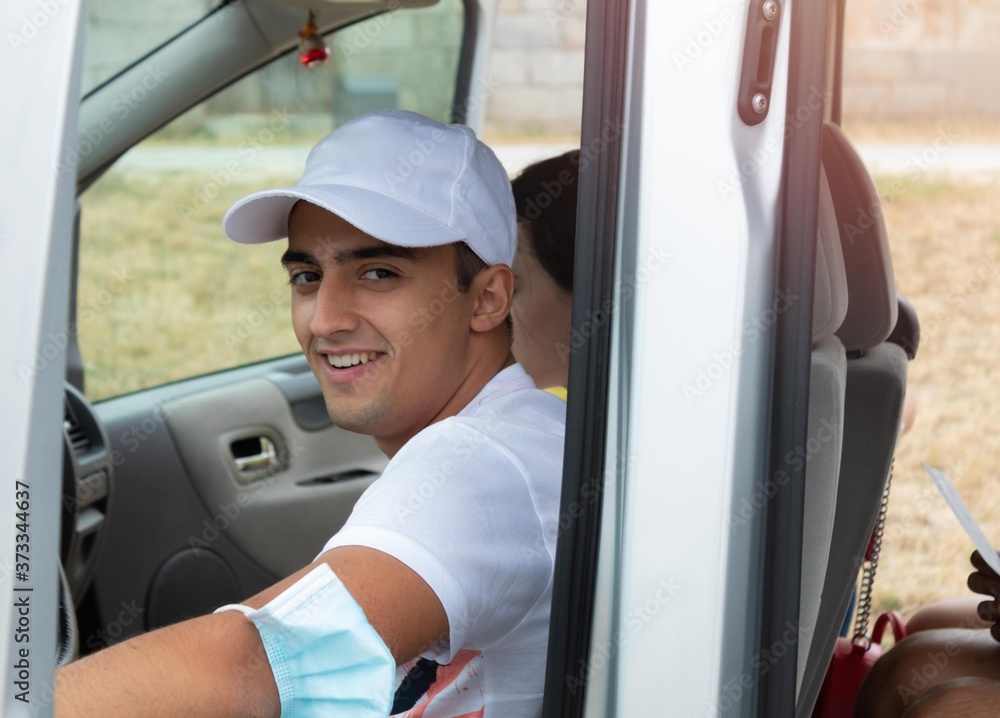 young teenage boy smiling in the car, ready to drive a trip with the family and wearing the health mask on his elbow young teenage boy smiling in the car, ready to drive a trip with the family and wearing the health mask on his elbow
