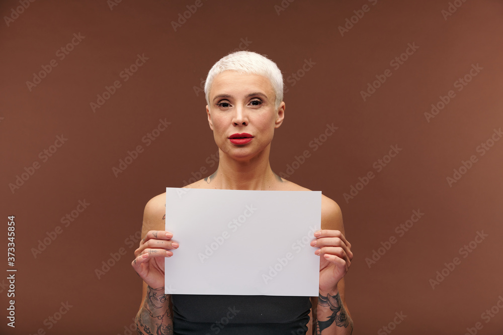 Contemporary young blond businesswoman with tattoos on arms holding blank paper Contemporary young blond businesswoman with tattoos on arms holding blank paper