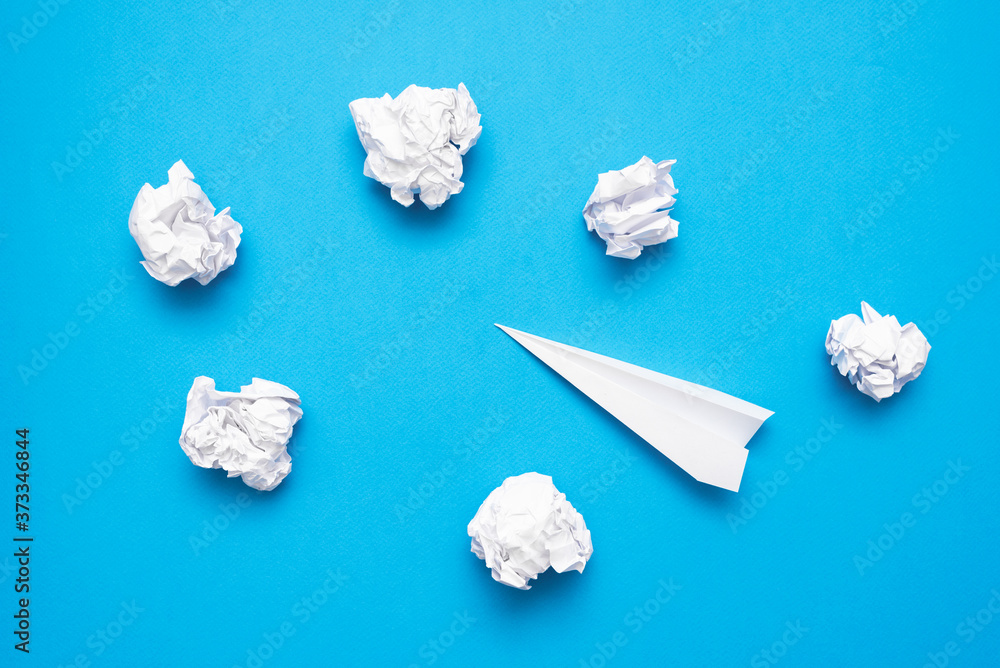 Obraz premium Paper plane and paper crumpled ball on the blue flat lay background.
