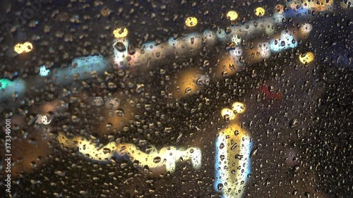 The rain drops flow down the glass on a background of city lights