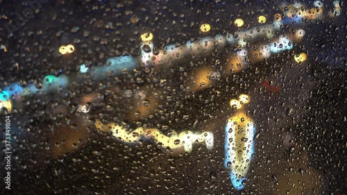 City Lights and Traffic on a Rainy Night - Rack Focus. Raindrops On Glass Window Against Night City Street During Thunderstorm. City Through Rainy Window
