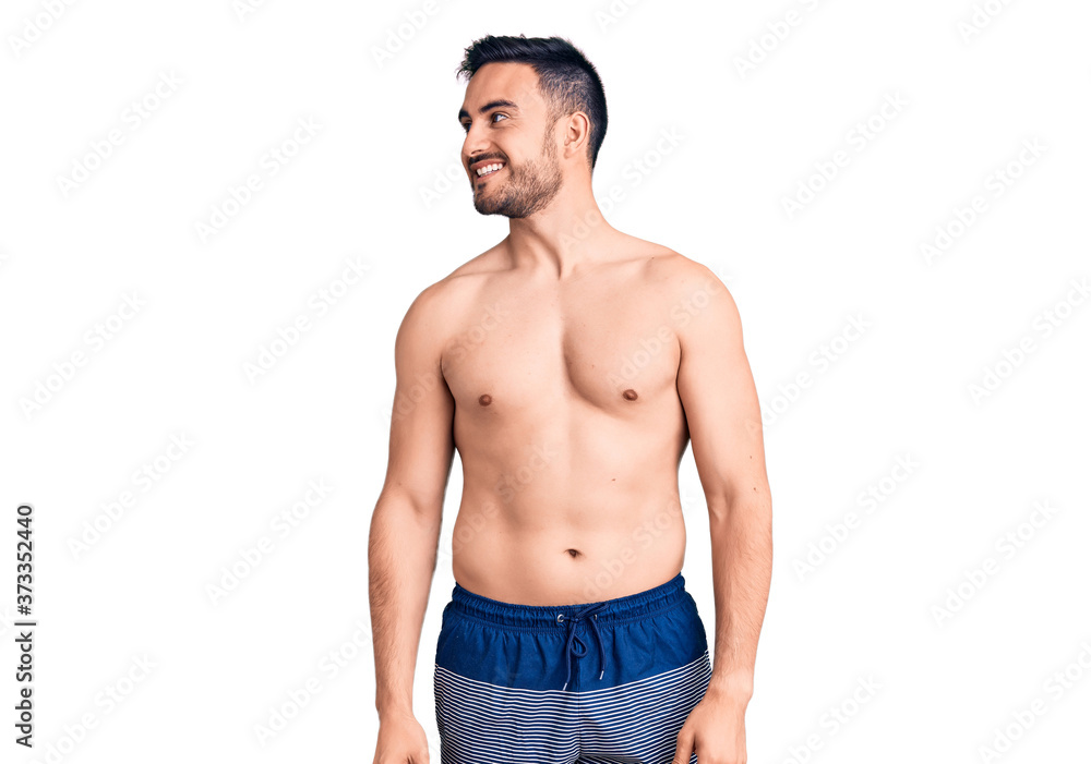 Young handsome man wearing swimwear looking away to side with smile on face, natural expression. laughing confident. Young handsome man wearing swimwear looking away to side with smile on face, natural expression. laughing confident.