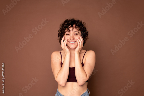 Happy young beautiful woman with short dark curly hair keeping her hands by face