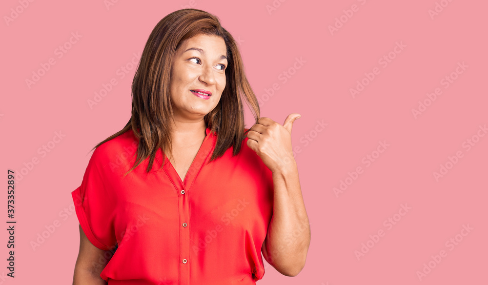 Middle age latin woman wearing casual clothes smiling with happy face looking and pointing to the side with thumb up. Middle age latin woman wearing casual clothes smiling with happy face looking and pointing to the side with thumb up.