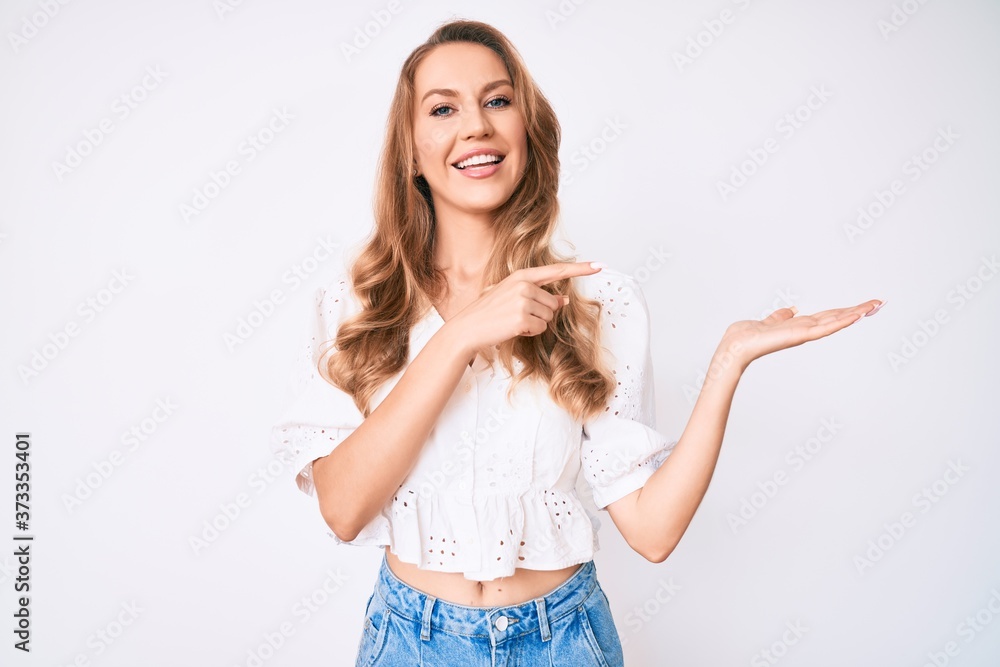 Young caucasian woman with blond hair wearing casual summer clothes amazed and smiling to the camera while presenting with hand and pointing with finger. Young caucasian woman with blond hair wearing casual summer clothes amazed and smiling to the camera while presenting with hand and pointing with finger.