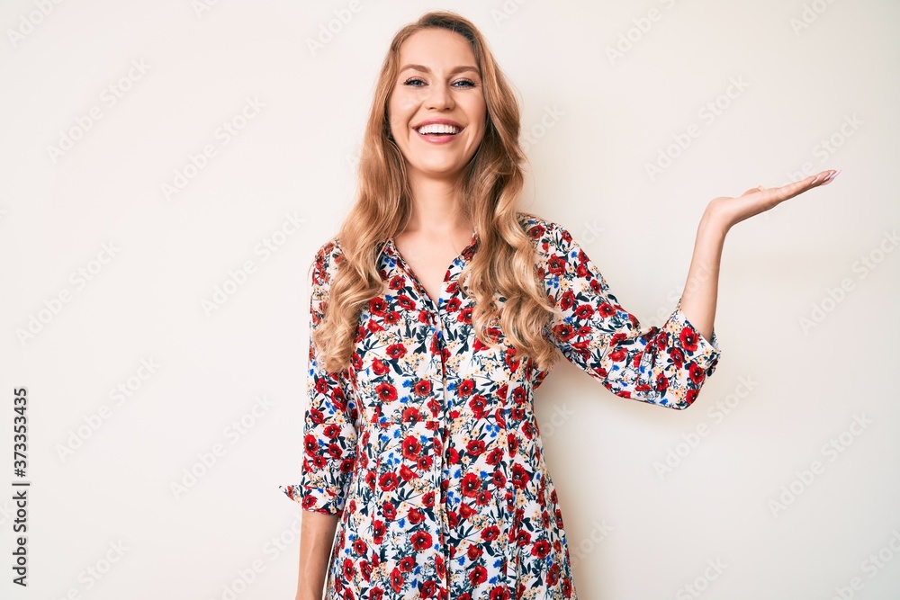 Young caucasian woman with blond hair wearing summer dress smiling cheerful presenting and pointing with palm of hand looking at the camera. Young caucasian woman with blond hair wearing summer dress smiling cheerful presenting and pointing with palm of hand looking at the camera.