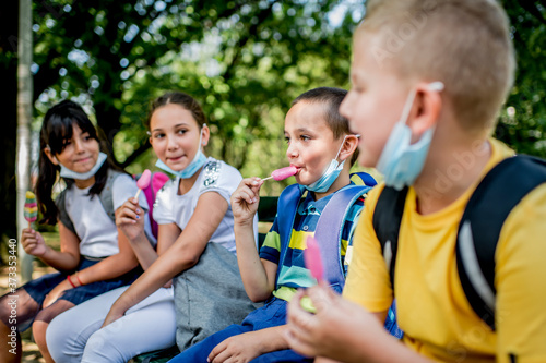 Group of children eating ice cream outside. They are wearing a protective face mask down.