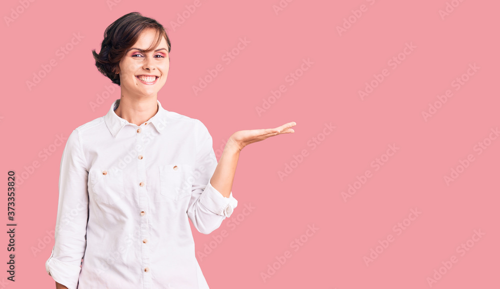 Beautiful young woman with short hair wearing elegant white shirt smiling cheerful presenting and pointing with palm of hand looking at the camera. Beautiful young woman with short hair wearing elegant white shirt smiling cheerful presenting and pointing with palm of hand looking at the camera.