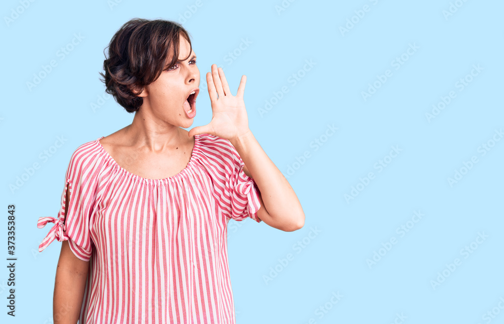 Beautiful young woman with short hair wearing casual summer clothes shouting and screaming loud to side with hand on mouth. communication concept. Beautiful young woman with short hair wearing casual summer clothes shouting and screaming loud to side with hand on mouth. communication concept.