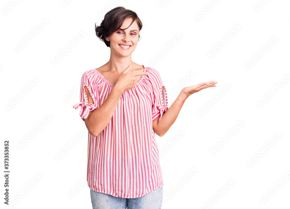 Beautiful young woman with short hair wearing casual summer clothes amazed and smiling to the camera while presenting with hand and pointing with finger. Beautiful young woman with short hair wearing casual summer clothes amazed and smiling to the camera while presenting with hand and pointing with finger.