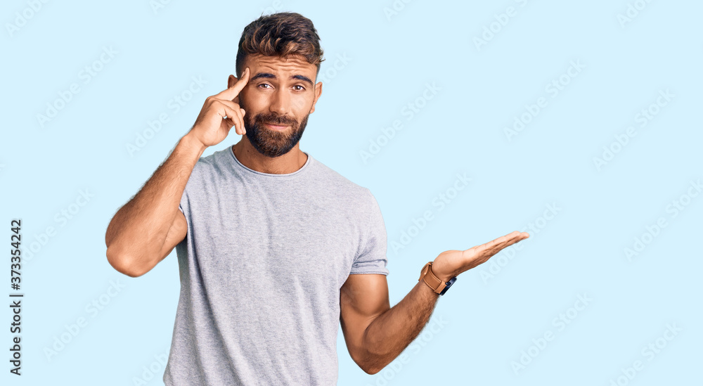 Young hispanic man wearing casual clothes confused and annoyed with open palm showing copy space and pointing finger to forehead. think about it. Young hispanic man wearing casual clothes confused and annoyed with open palm showing copy space and pointing finger to forehead. think about it.