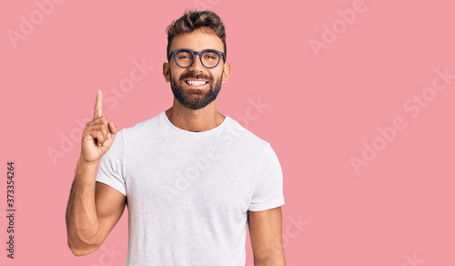 Young hispanic man wearing casual clothes and glasses showing and pointing up with finger number one while smiling confident and happy. photo