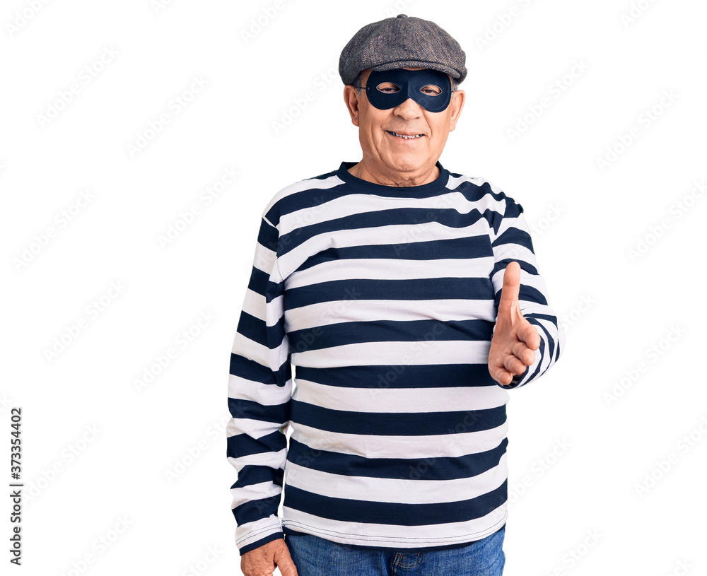 Senior handsome man wearing burglar mask and t-shirt smiling cheerful offering palm hand giving assistance and acceptance. Senior handsome man wearing burglar mask and t-shirt smiling cheerful offering palm hand giving assistance and acceptance.