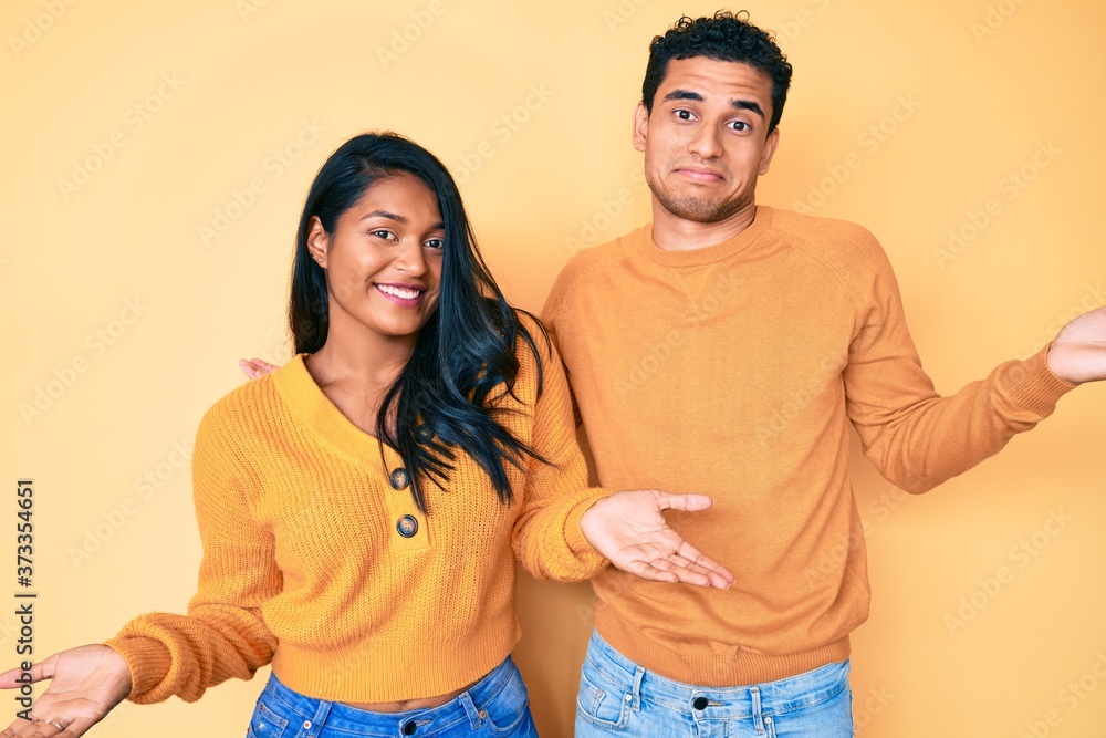 Fototapeta premium Beautiful latin young couple wearing casual clothes together smiling showing both hands open palms, presenting and advertising comparison and balance