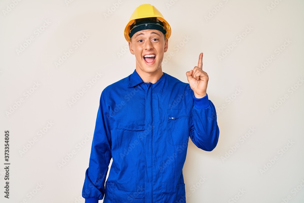 Young hispanic boy wearing worker uniform and hardhat pointing finger up with successful idea. exited and happy. number one.