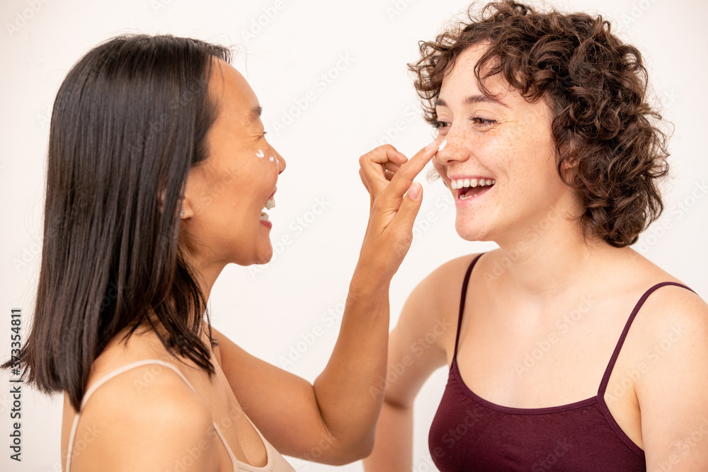 Two young laughing intercultural brunettes having fun during skincare procedure Two young laughing intercultural brunettes having fun during skincare procedure