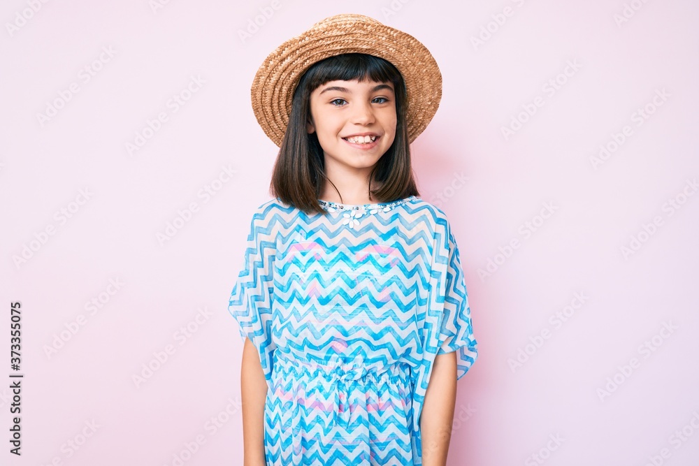 Young little girl with bang wearing summer dress and hat looking positive and happy standing and smiling with a confident smile showing teeth Young little girl with bang wearing summer dress and hat looking positive and happy standing and smiling with a confident smile showing teeth