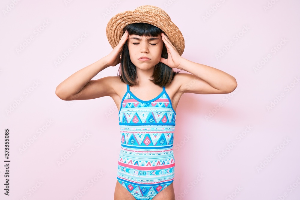 Young little girl with bang wearing swimsuit and summer hat with hand on head, headache because stress. suffering migraine. Young little girl with bang wearing swimsuit and summer hat with hand on head, headache because stress. suffering migraine.
