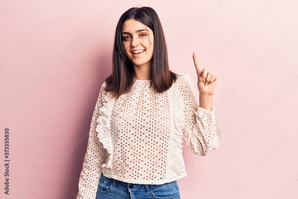 Young beautiful girl wearing casual t shirt smiling with an idea or question pointing finger up with happy face, number one