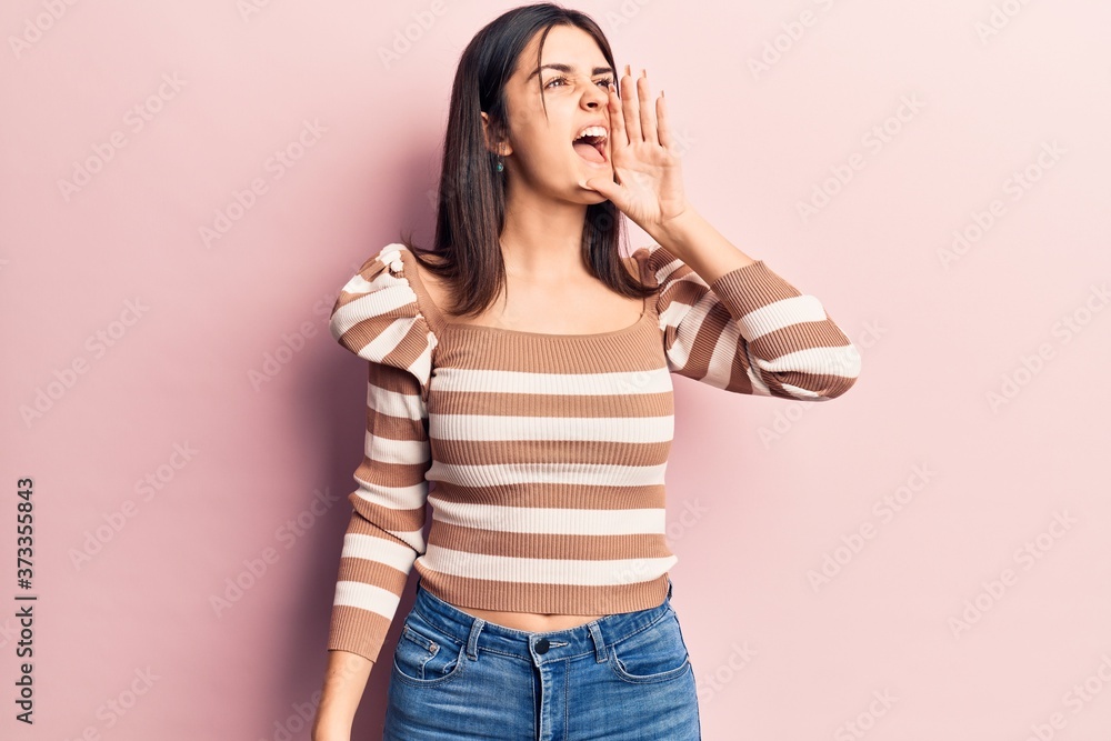 Young beautiful girl wearing casual striped t shirt shouting and screaming loud to side with hand on mouth. communication concept. Young beautiful girl wearing casual striped t shirt shouting and screaming loud to side with hand on mouth. communication concept.
