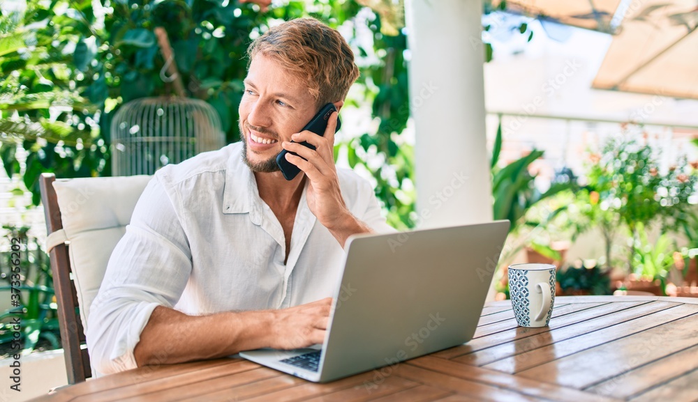 Handsome caucasian man sitting on the terrace working from home using computer laptop and speaking on the phone Handsome caucasian man sitting on the terrace working from home using computer laptop and speaking on the phone