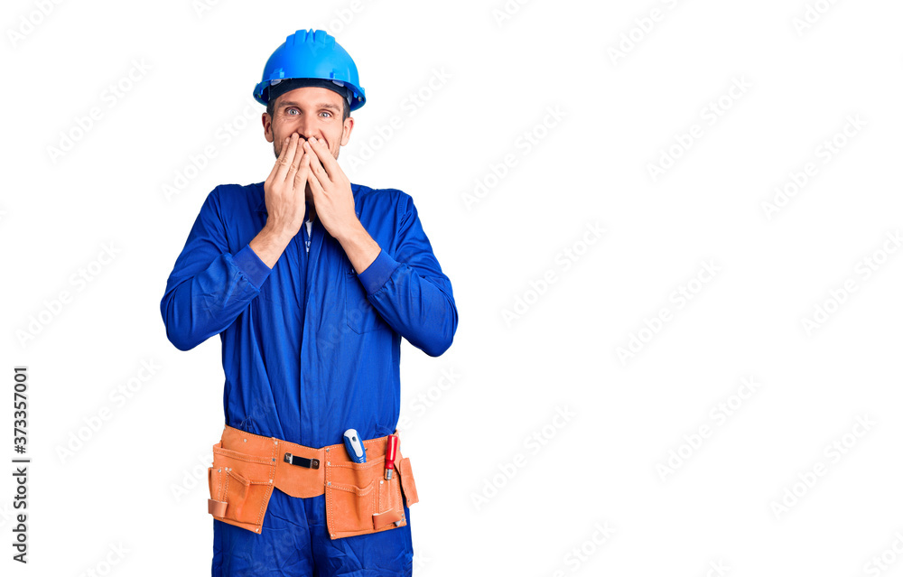 Young handsome man wearing worker uniform and hardhat laughing and embarrassed giggle covering mouth with hands, gossip and scandal concept