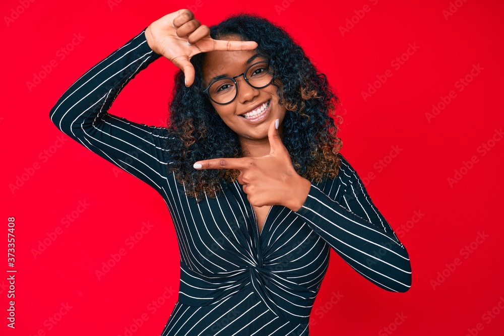 Young african american woman wearing casual clothes and glasses smiling making frame with hands and fingers with happy face. creativity and photography concept. Young african american woman wearing casual clothes and glasses smiling making frame with hands and fingers with happy face. creativity and photography concept.