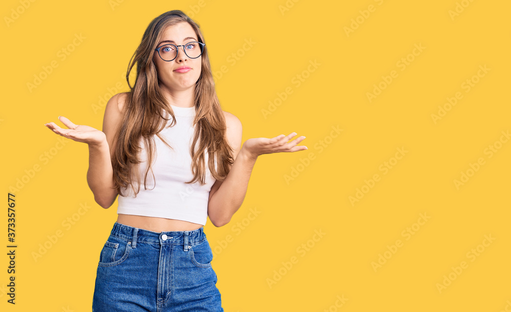 Beautiful caucasian young woman wearing casual clothes and glasses clueless and confused expression with arms and hands raised. doubt concept. Beautiful caucasian young woman wearing casual clothes and glasses clueless and confused expression with arms and hands raised. doubt concept.