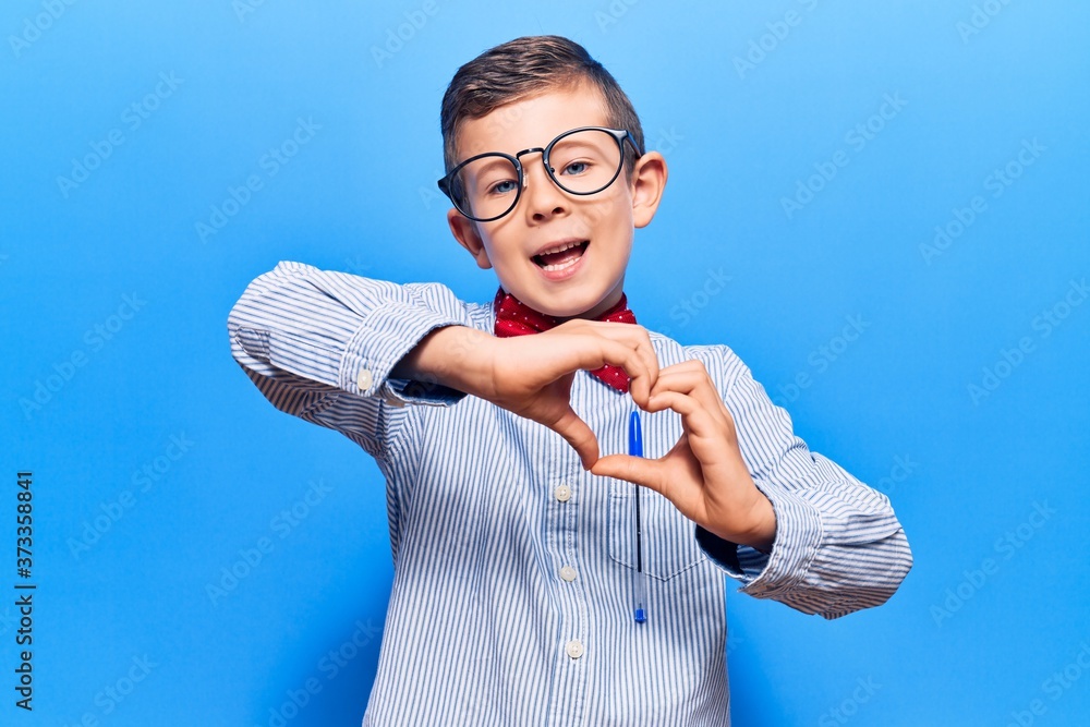 Fototapeta premium Cute blond kid wearing nerd bow tie and glasses smiling in love doing heart symbol shape with hands. romantic concept.
