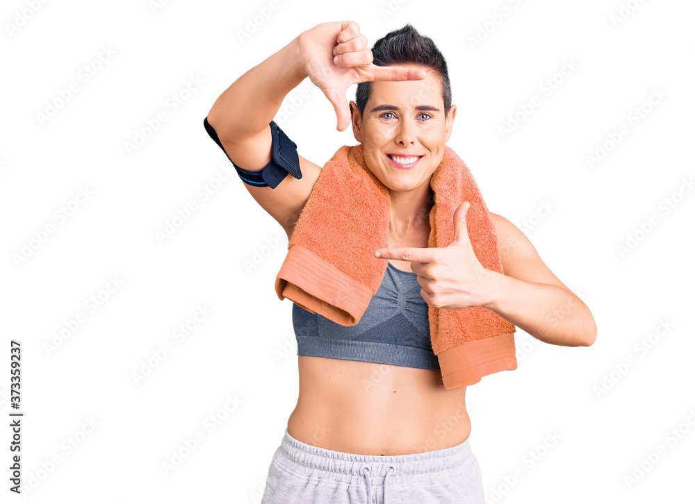 Young woman with short hair wearing sportswear and towel using smartphone smiling making frame with hands and fingers with happy face. creativity and photography concept. Young woman with short hair wearing sportswear and towel using smartphone smiling making frame with hands and fingers with happy face. creativity and photography concept.