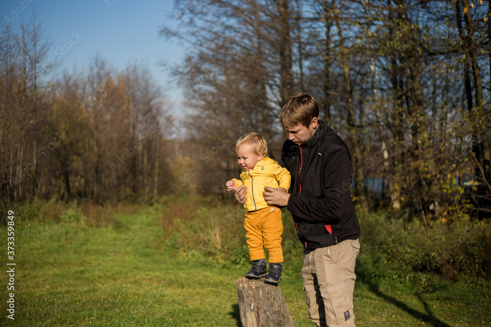 Little boy todler stands on a tree stump, dad supports him