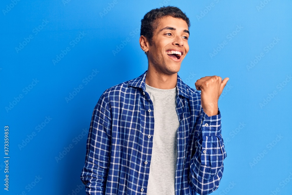 Young african amercian man wearing casual clothes pointing thumb up to the side smiling happy with open mouth Young african amercian man wearing casual clothes pointing thumb up to the side smiling happy with open mouth