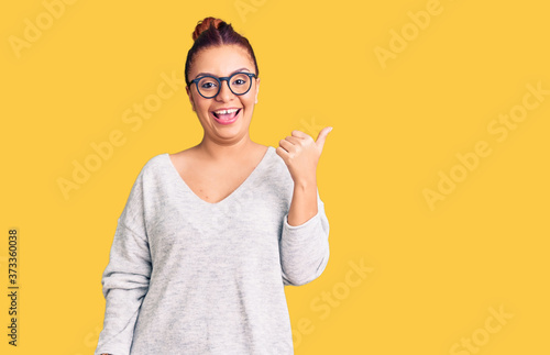 Young latin woman wearing casual clothes smiling with happy face looking and pointing to the side with thumb up.