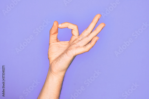 Hand of caucasian young man showing fingers over isolated purple background gesturing approval expression doing okay symbol with fingers