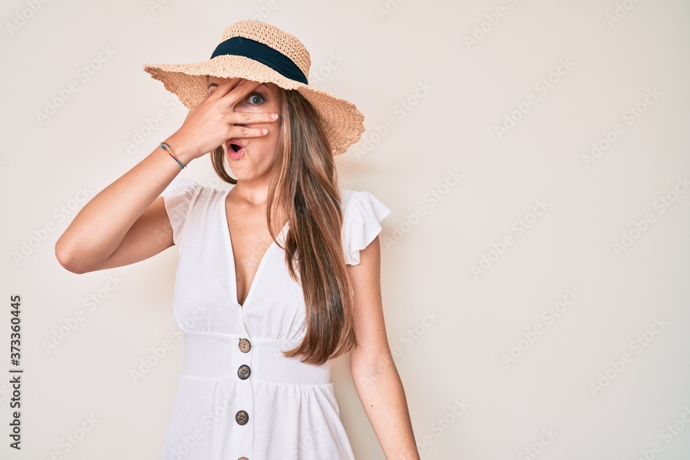 Young blonde girl wearing summer hat peeking in shock covering face and eyes with hand, looking through fingers afraid Young blonde girl wearing summer hat peeking in shock covering face and eyes with hand, looking through fingers afraid
