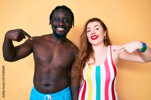 Interracial couple wearing swimwear looking confident with smile on face  pointing oneself with fingers proud and happy.
