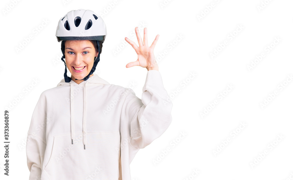 Beautiful brunette young woman wearing bike helmet and sporty clothes smiling and confident gesturing with hand doing small size sign with fingers looking and the camera. measure concept. Beautiful brunette young woman wearing bike helmet and sporty clothes smiling and confident gesturing with hand doing small size sign with fingers looking and the camera. measure concept.